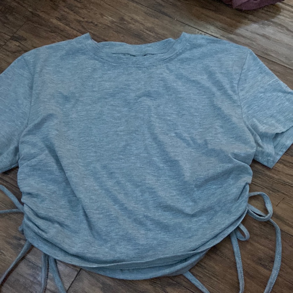 grey crop top with adjustable strings on both sides of the shirt.
